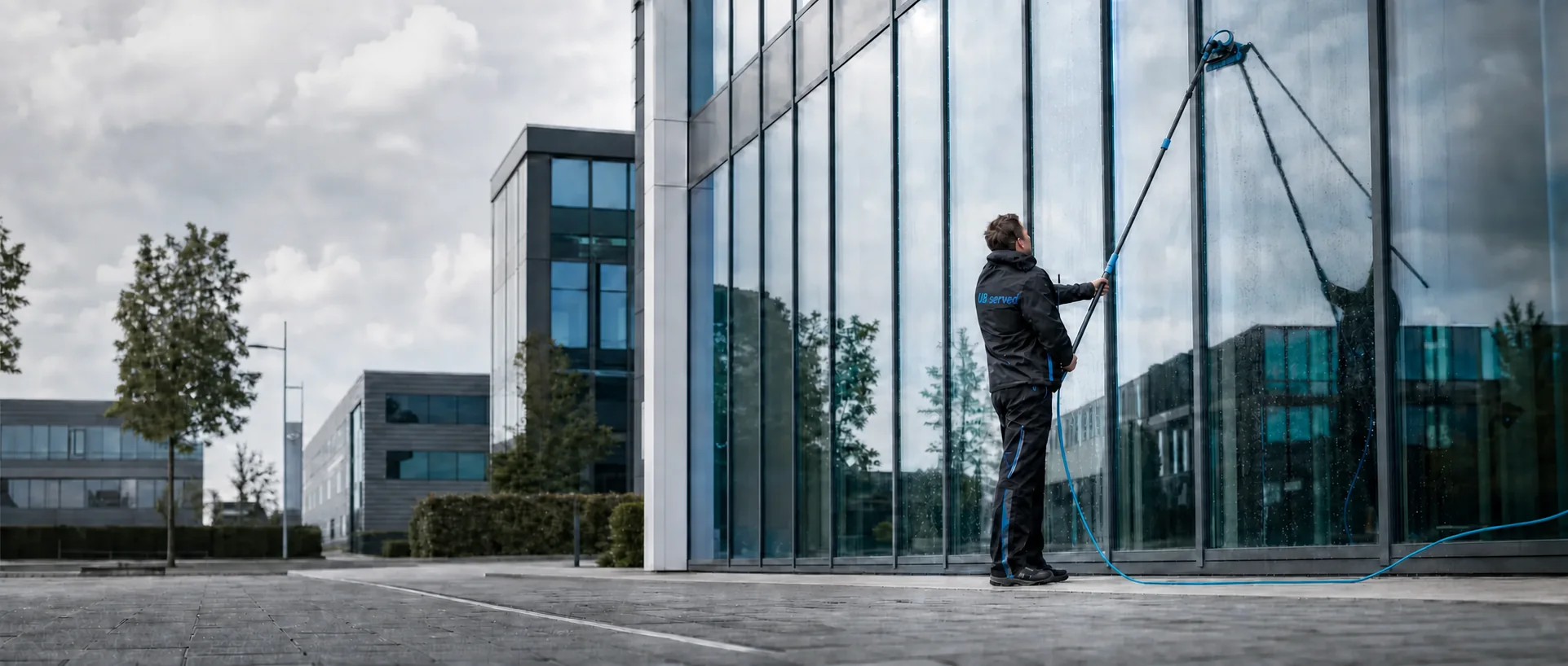 Mannelijke UB Served-specialist reinigt een glazen gevel met een telescoopsteel